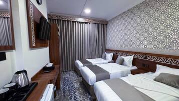 Quarto de hotel com duas camas, uma escrivaninha com chaleira e parede estampada.