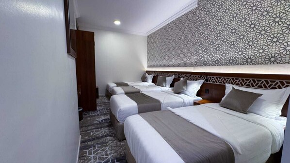 A hotel room with four beds, a patterned headboard, and a geometric carpet. - Golden Baron Hotel (Makkah)