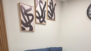 Sininen sohva, jossa on ulosvedettävä osa, on sijoitettu valkoisen seinän eteen, ja seinällä on näkyvillä abstraktia taidetta.