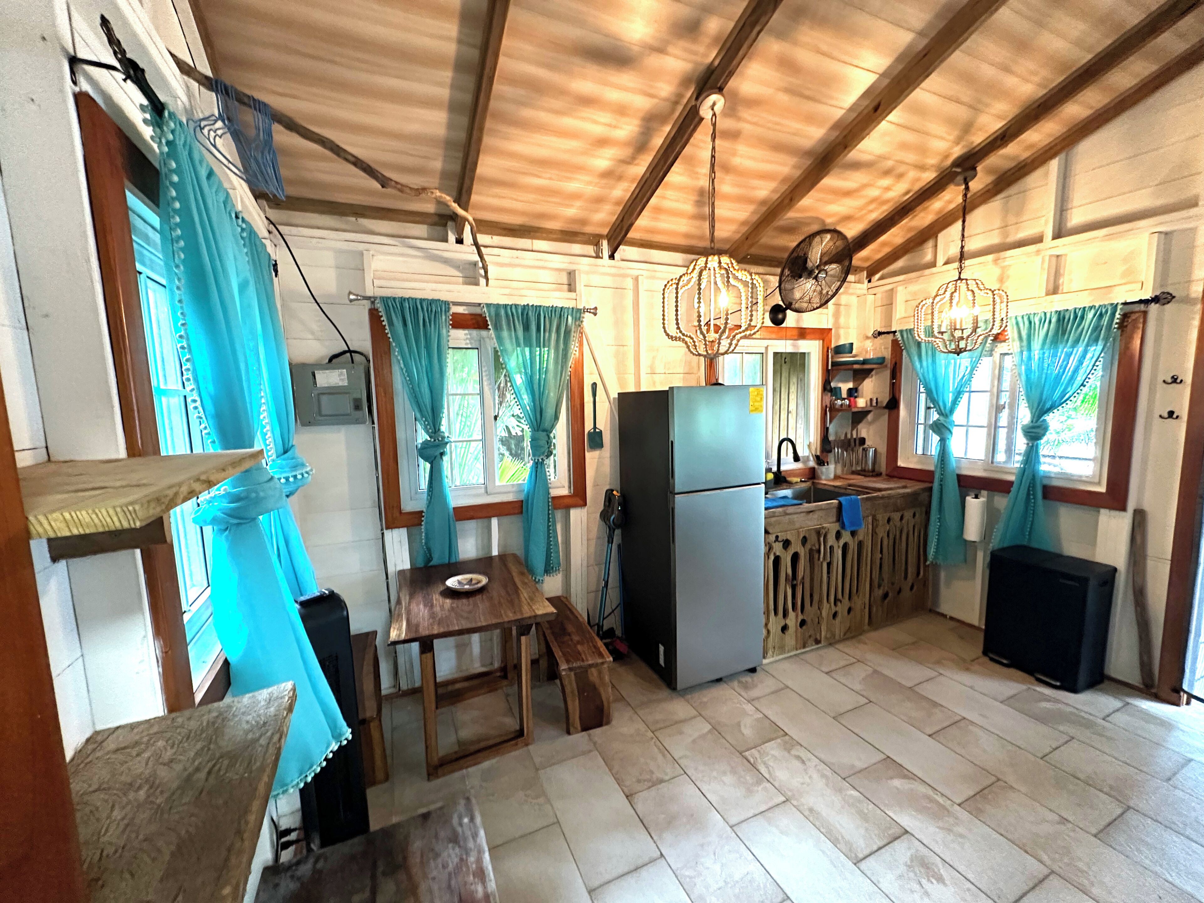A compact kitchen with a refrigerator, wooden table, and blue curtains.