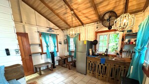 A kitchen with wooden cabinets, a refrigerator, a sink, and a dining area with benches. - SEA GLASS HOUSE: Waterfront, Caribbean Island Jungle Cabin in Bastimentos w/ AC (Bastimentos Island)