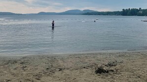 Una platja amb aigües tranquil·les, una persona banyant-se i turons lluny.