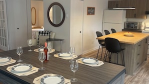Cuina moderna amb una illa central, zona de dinar amb una taula llarga per a sis comensals i un mirall gran a la paret.