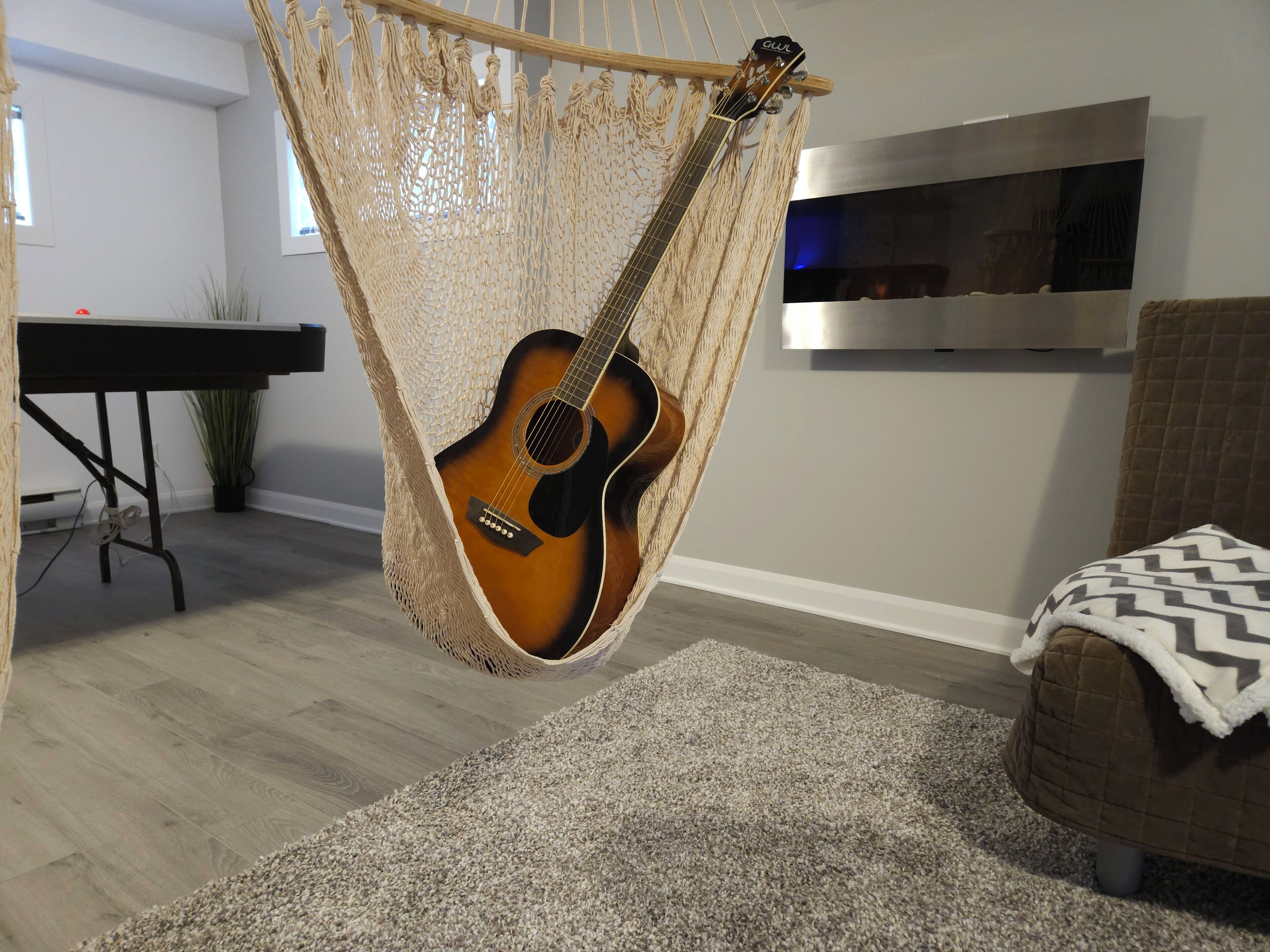 Un sillón hamaca junto a una guitarra, un televisor en la pared, un piano y un sofá con una manta.