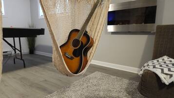 Un sillón hamaca junto a una guitarra, un televisor en la pared, un piano y un sofá con una manta.