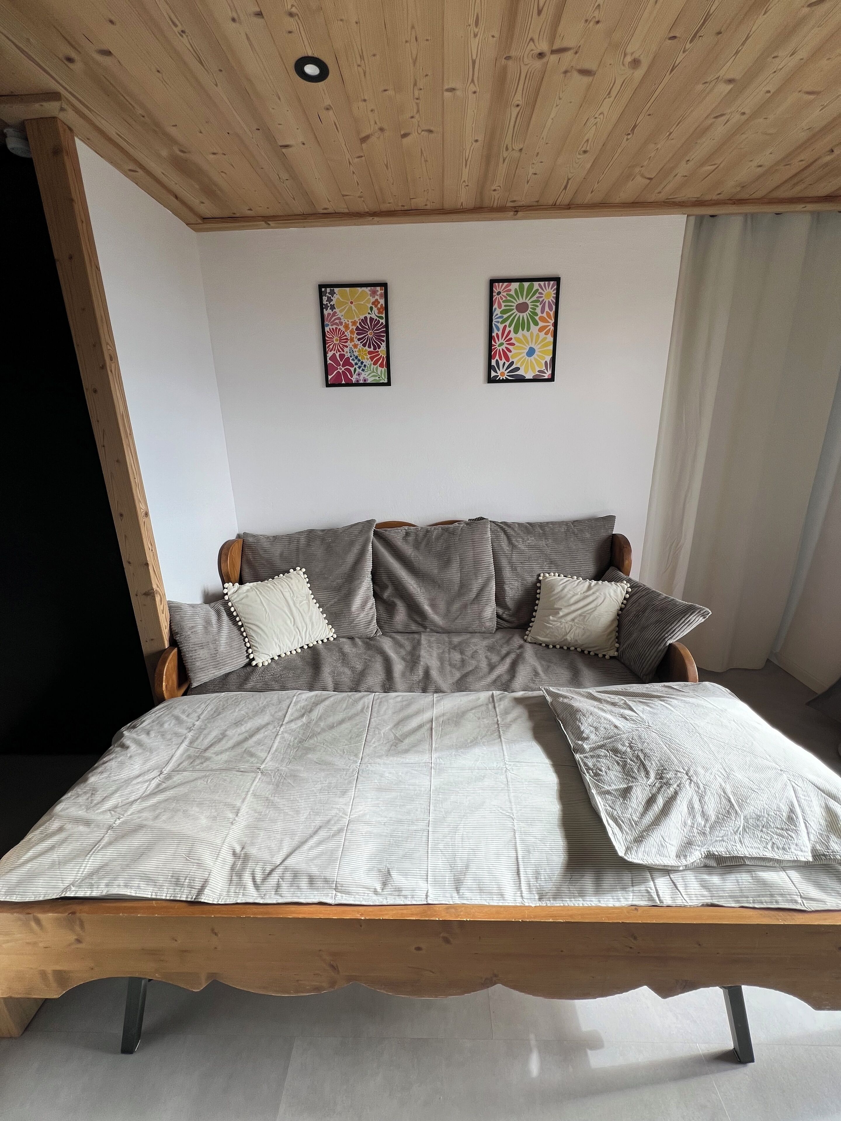 A bedroom with a wooden bed frame, grey bedding, and two floral wall art pieces.