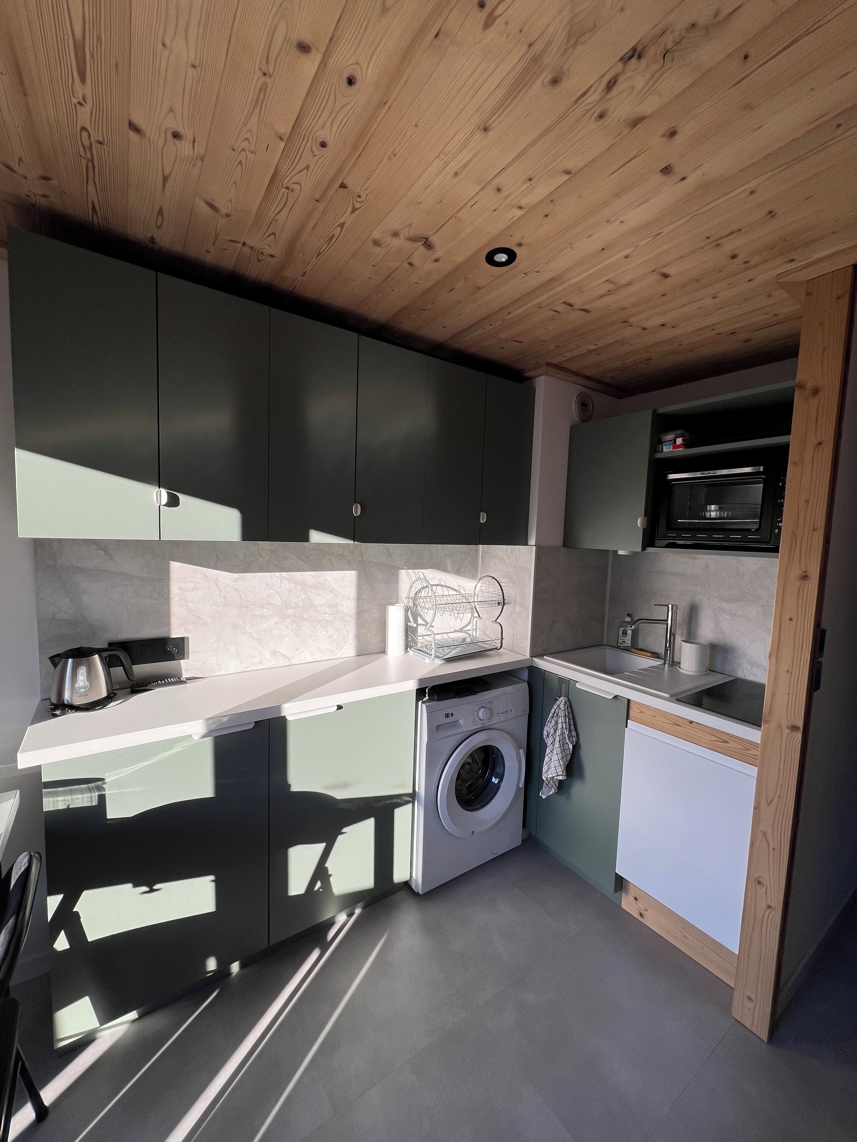Una cucina compatta con mobili scuri, una lavatrice integrata, un forno a microonde e un lavello.