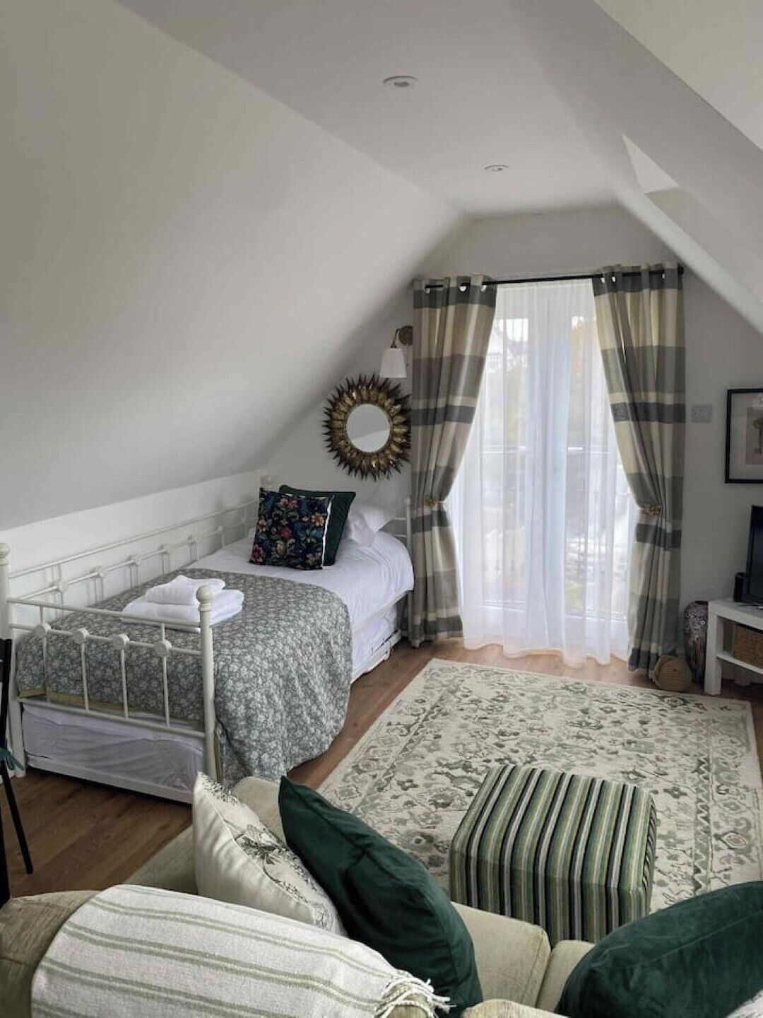 Une chambre à coucher avec un lit, une table de chevet, un miroir et une fenêtre avec des rideaux.
