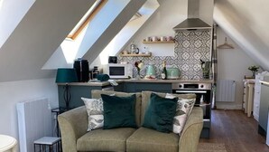 A loft-style living space with a high ceiling, a kitchenette, a sofa set, and a patterned rug. - Grove View Studio Apartment. (Cossington)