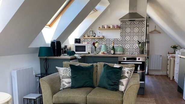 A loft-style living space with a high ceiling, a kitchenette, a sofa set, and a patterned rug. - Grove View Studio Apartment. (Cossington)
