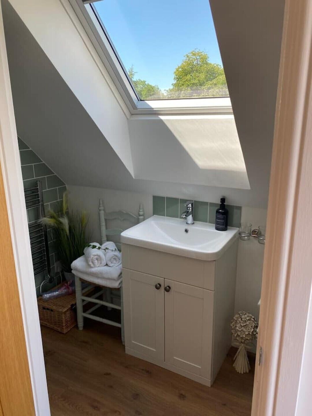 A small, modern bathroom with a skylight, a white sink, and a wooden floor.