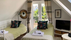 A cozy room with two beds, a TV, and a balcony with curtains. - Grove View Studio Apartment. (Cossington)