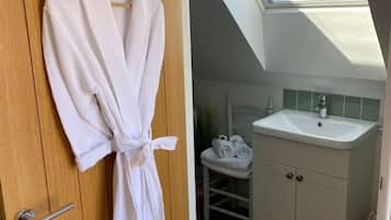 A room with a wooden door, a white robe hanging on it, a skylight, a white sink, and a small white chair.