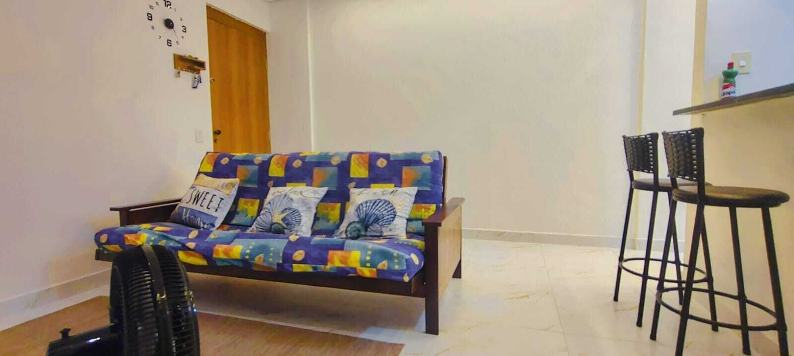 Un salon avec un canapé, deux tabourets de bar noirs, une petite table et une horloge murale.
