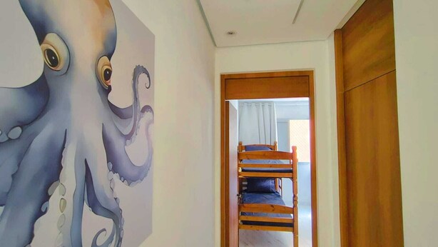 A room with a bunk bed, a wooden door, and a large octopus mural on the wall. - Apartment with pool, just a 9-minute walk from the beach! (Guarujá)
