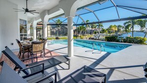 A pool area with lounge chairs, a table, and a view of the ocean.