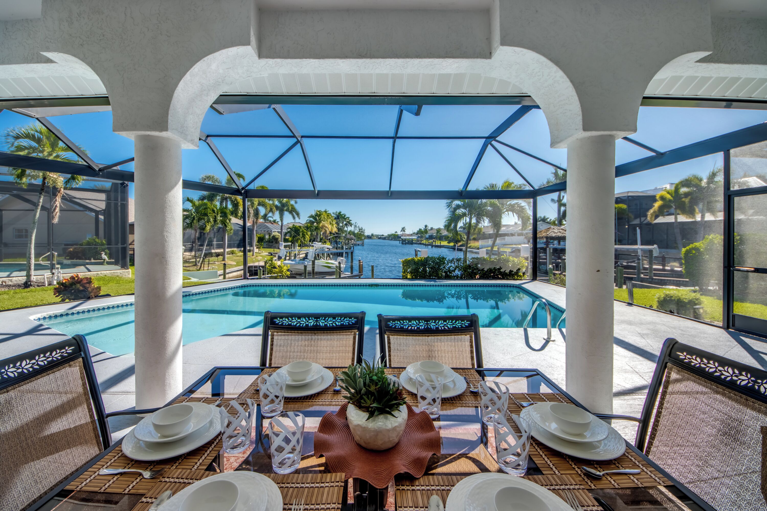 A poolside dining area with a view of a large pool and palm trees.