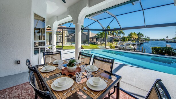 A dining area with a table set for four, overlooking a pool and marina.