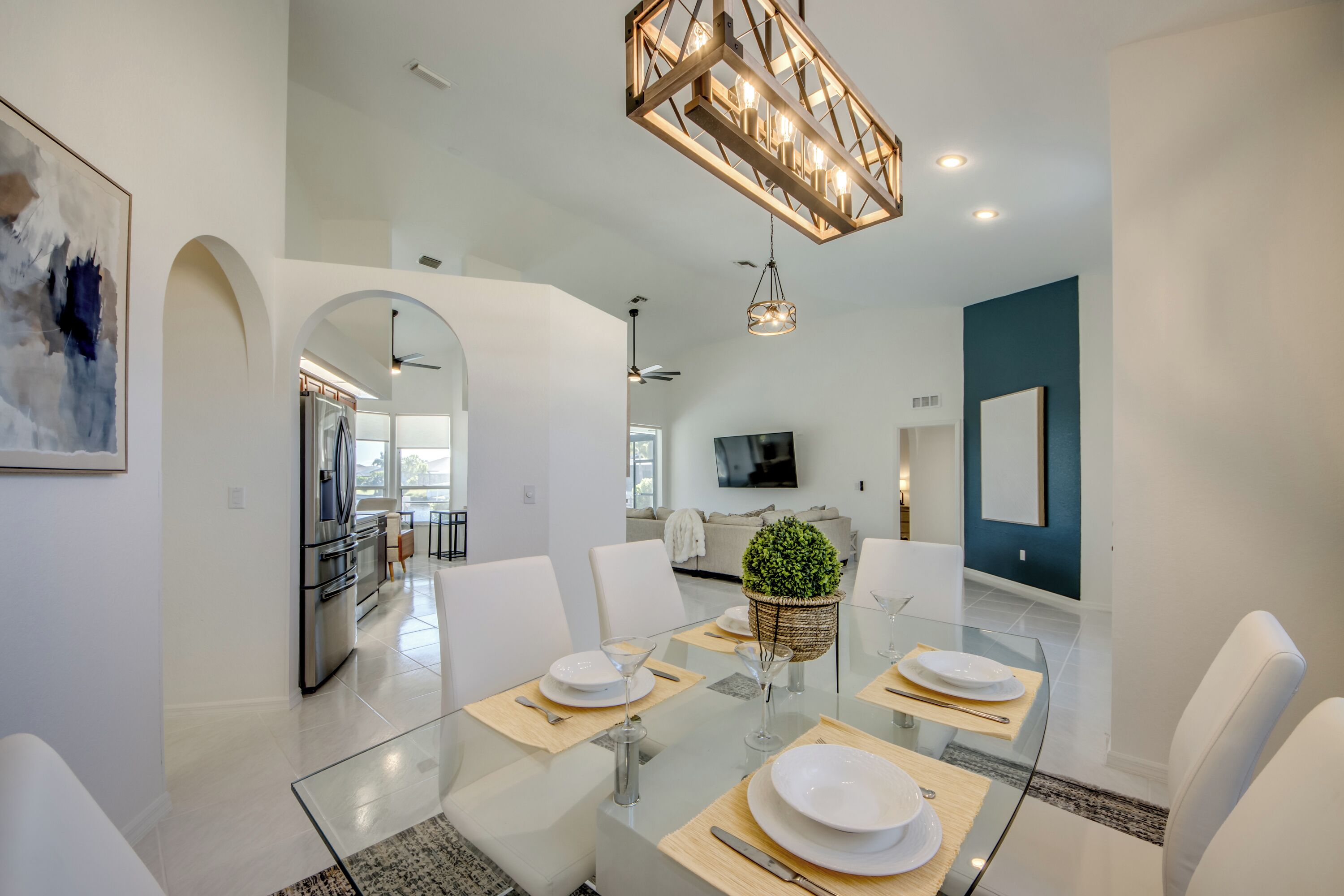 A modern dining area with a glass table, white chairs, and a chandelier.