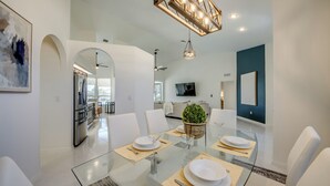 A modern dining area with a glass table, white chairs, and a chandelier.