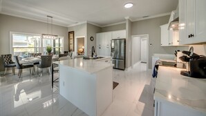 A spacious kitchen with white cabinetry, a central island, and a dining area with chairs and a table. - Villa Sunset Retreat - Modern 4 BR/ 2 bath waterfront Villa w. heated pool / boat dock/ direct access (Cape Coral)