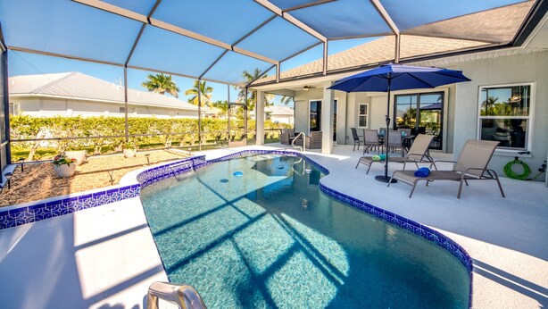 A covered swimming pool with lounge chairs and a patio area. - Villa Sunset Retreat - Modern 4 BR/ 2 bath waterfront Villa w. heated pool / boat dock/ direct access (Cape Coral)