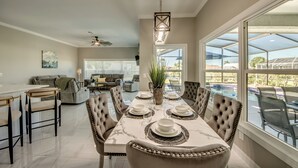 A dining area with a marble table, upholstered chairs, and a hanging light fixture. - Villa Sunset Retreat - Modern 4 BR/ 2 bath waterfront Villa w. heated pool / boat dock/ direct access (Cape Coral)