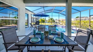 An outdoor dining area with a table set for four, overlooking a swimming pool and a view of the surrounding landscape. - Villa Sunset Retreat - Modern 4 BR/ 2 bath waterfront Villa w. heated pool / boat dock/ direct access (Cape Coral)