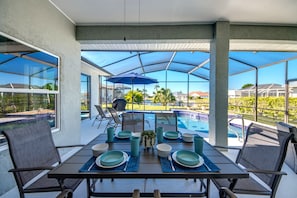 An outdoor dining area with a table set for four, overlooking a swimming pool and a view of the surrounding landscape.