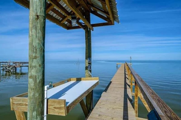 A wooden pier extending into calm water, with a bench and a covered area at the end.