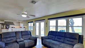 Un salon avec deux canapés sombres, un ventilateur de plafond et de grandes fenêtres offrant une belle vue.