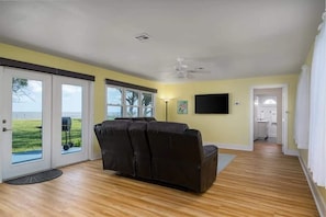A living room with a sofa, a ceiling fan, and a view through a sliding glass door.