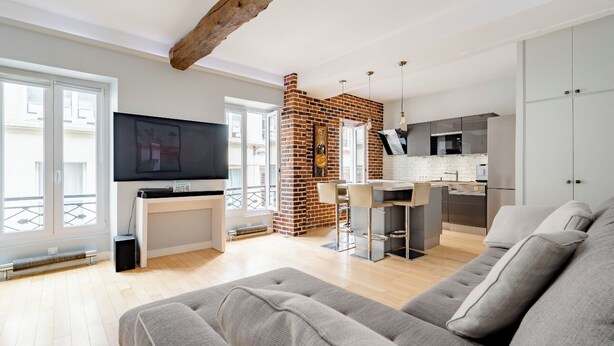 A modern living room with a grey sofa, a flat-screen TV, and a brick fireplace. - Chic apartment in the heart of Montmartre Parisian charm & central calm (Paris)
