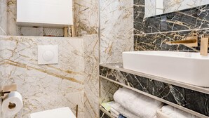 A bathroom with a toilet, sink, and marble walls. - Chic apartment in the heart of Montmartre Parisian charm & central calm (Paris)
