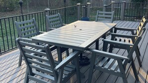 Een houten terras met een tafel en stoelen, omringd door een metalen hek en bomen.