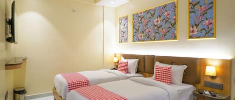 Habitación de hotel con dos camas, ventilador de techo, televisor y cuadros con motivos florales en las paredes.