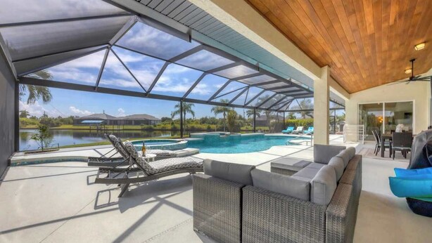Un espacio al aire libre techado con piscina, sillones de descanso y una zona de estar con vista a un lago y palmeras.