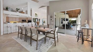 Una cocina moderna con armarios blancos, un comedor con mesa y sillas de madera, y un ventilador de techo.