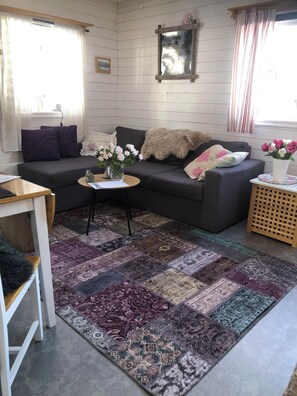 A cozy living room with a dark grey sofa, a patterned rug, and a small side table with a vase of flowers. - Villa Stuga (Hammarstrand)
