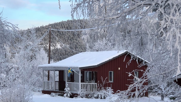 A snow-covered cabin with a porch and a flag.