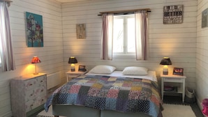 A cozy bedroom with a bed, two bedside tables, a nightstand, a dresser, a window with curtains, and a wall with a motivational quote.