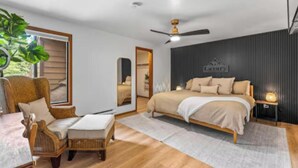 Ein Schlafzimmer mit einem Kingsize-Bett, einem Sessel, einem kleinen Tisch, einer Pflanze und einem Deckenventilator.