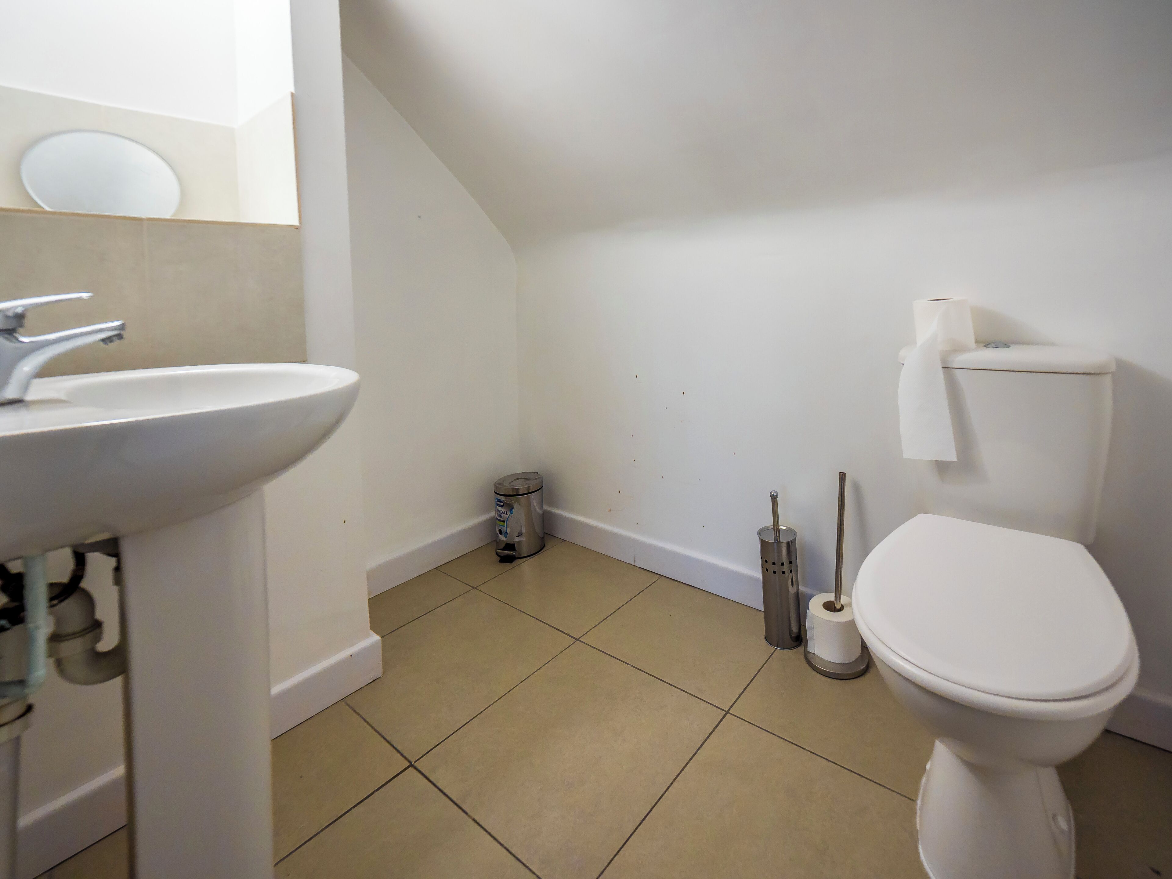 A bathroom with a white sink, toilet, and a trash can.
