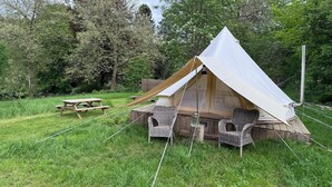 Une tente, une table de pique-nique et des chaises en osier, le tout installé dans un espace herbeux.
