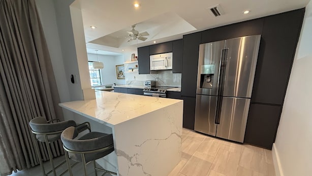 A modern kitchen with a marble island, stainless steel appliances, and a ceiling fan. - 3/2 Luxury Waterfront Pool Home (Punta Gorda)