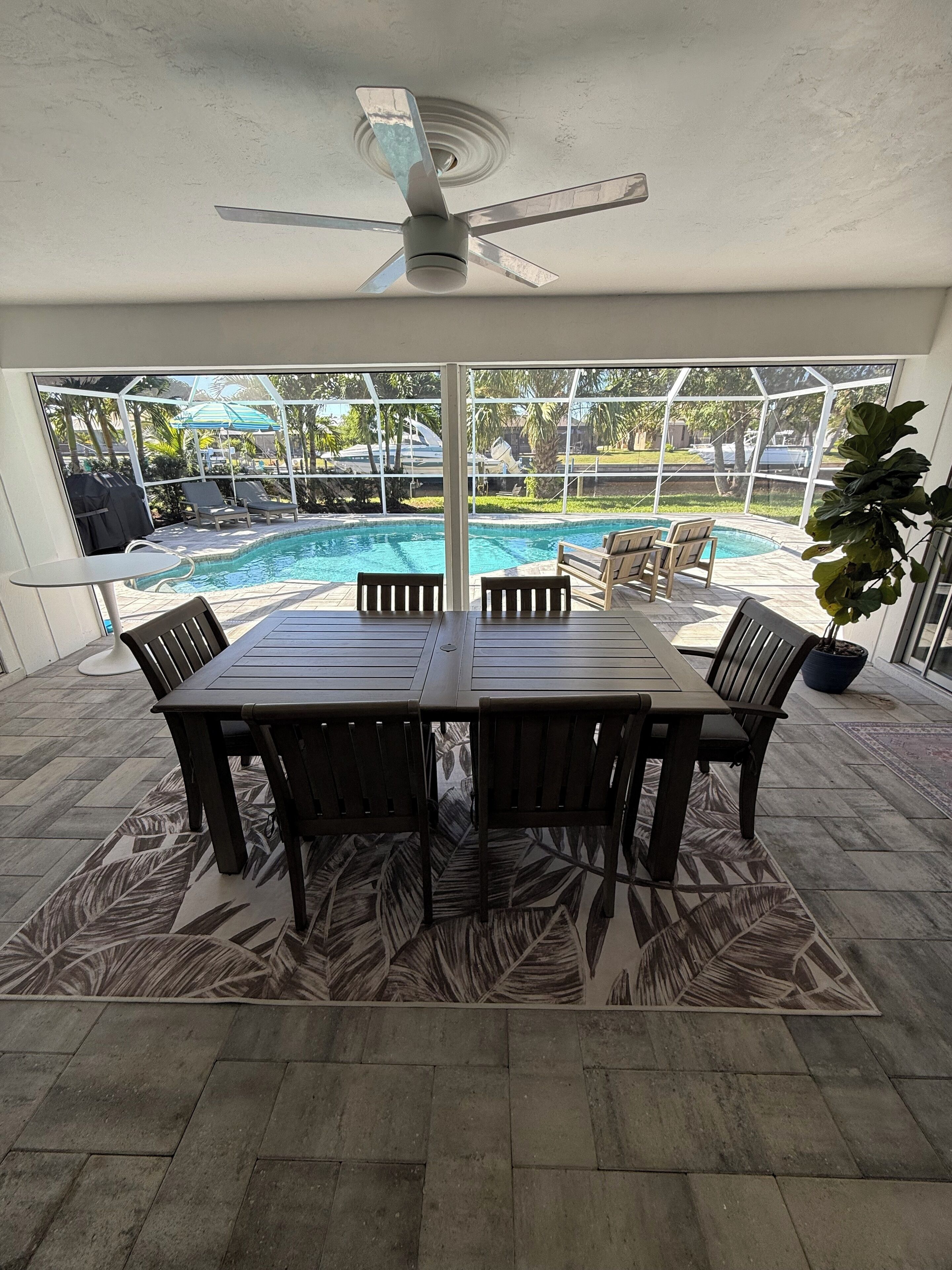 A poolside dining area with a table and chairs, a ceiling fan, and a view of a swimming pool.