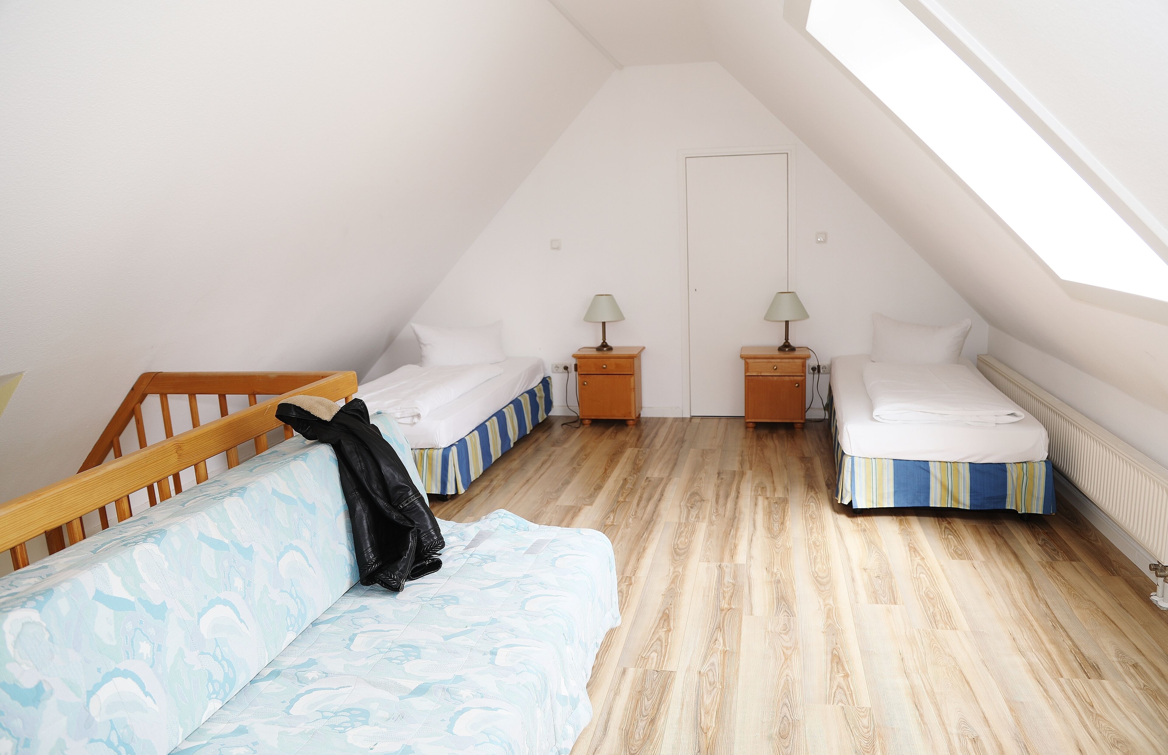Ein kleines, helles Schlafzimmer im Dachgeschoss mit zwei Einzelbetten, einer hölzernen Sitzbank und einem Dachfenster.