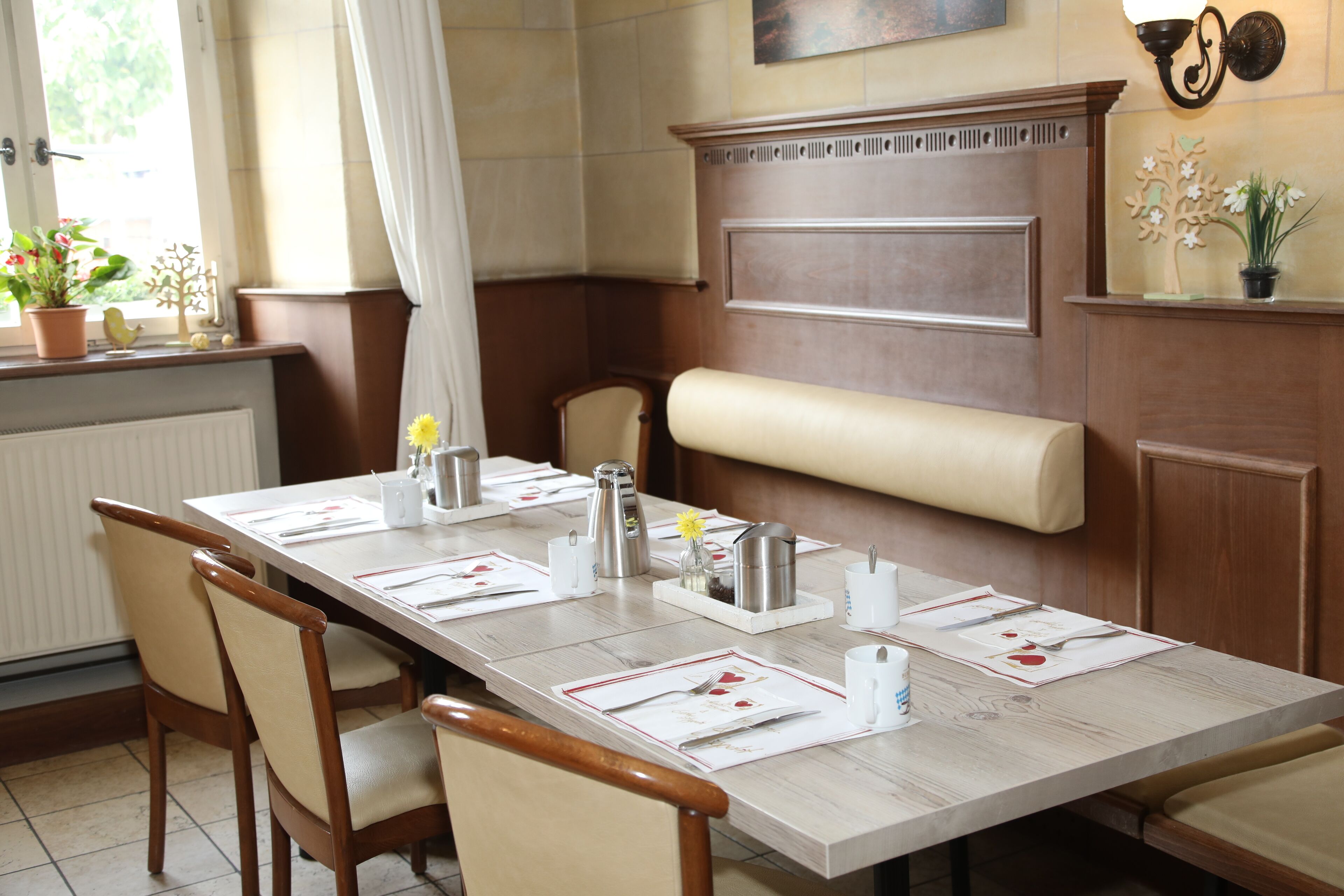Un espace repas avec une longue table dressée pour plusieurs personnes, des chaises, un banc et un radiateur.