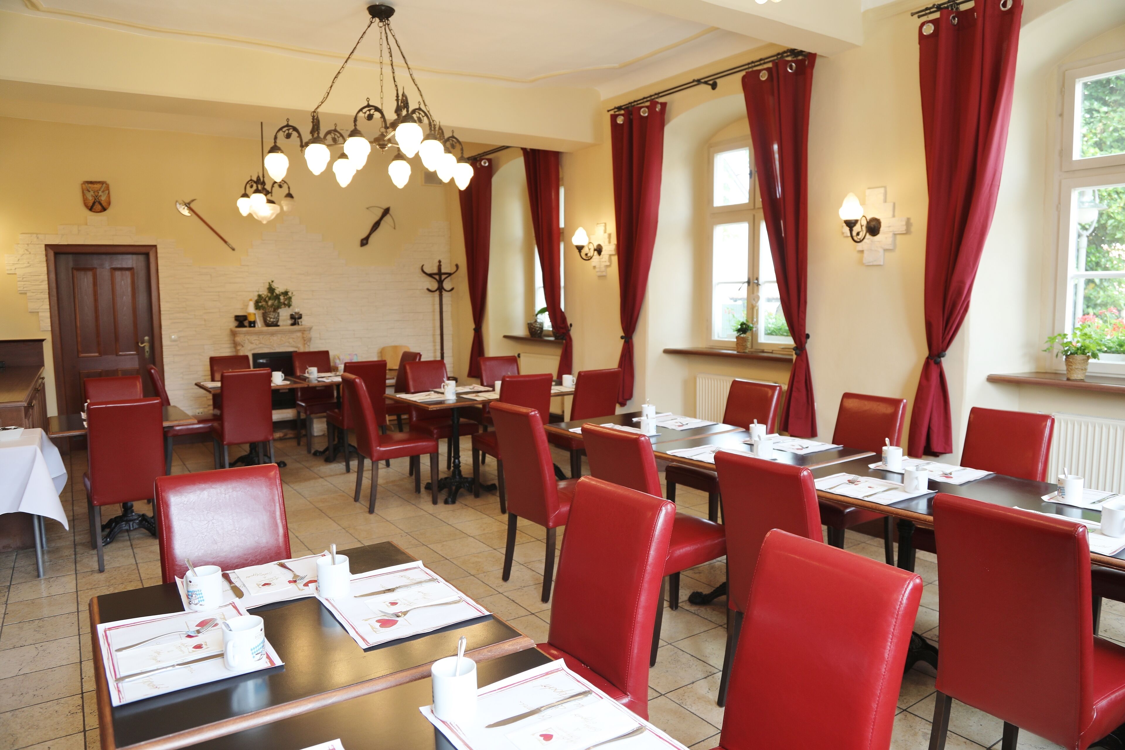 A dining area with red chairs and tables, a chandelier, and red curtains.