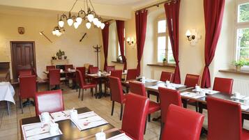A dining area with red chairs and tables, a chandelier, and red curtains.